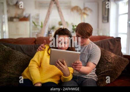 Young Downs Syndrome Couple Sitting On Sofa Using Digital Tablet At Home Stock Photo