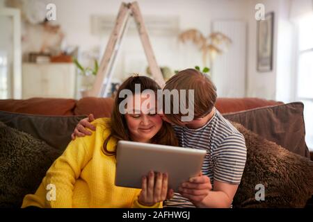 Loving Young Downs Syndrome Couple Sitting On Sofa Using Digital Tablet At Home Stock Photo