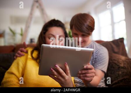 Young Downs Syndrome Couple Sitting On Sofa Using Digital Tablet At Home Stock Photo