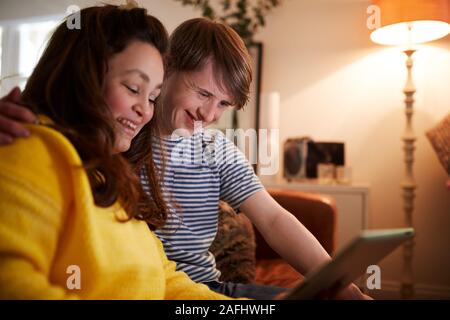 Young Downs Syndrome Couple Sitting On Sofa Using Digital Tablet At Home Stock Photo