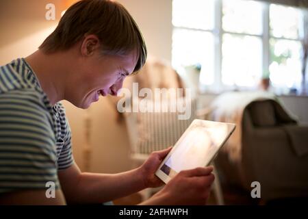 Young Downs Syndrome Man Sitting On Sofa Using Digital Tablet At Home Stock Photo
