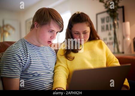Young Downs Syndrome Couple Sitting On Sofa Using Laptop At Home Stock Photo