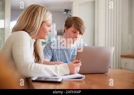 Downs Syndrome Man Sitting With Home Tutor Using Laptop For Lesson At Home Stock Photo