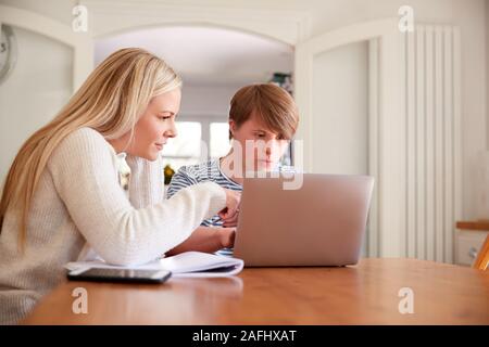 Downs Syndrome Man Sitting With Home Tutor Using Laptop For Lesson At Home Stock Photo
