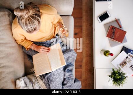 Overhead Shot Looking Down On Woman At Home Lying On Reading Book And Drinking Wine Stock Photo