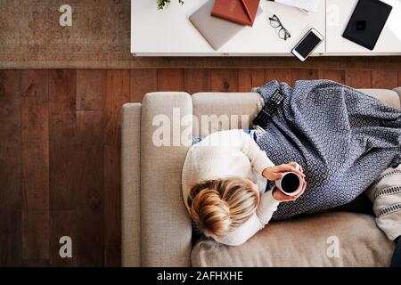 Overhead Shot Looking Down On Woman At Home Lying On Sofa Watching Television Stock Photo