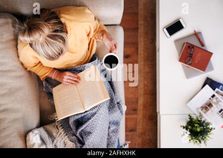 Overhead Shot Looking Down On Woman At Home Lying On Reading Book And Drinking Coffee Stock Photo