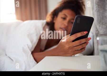 Woman Waking Up In Bed Immediately Reaches Out To Look At Mobile Phone Stock Photo