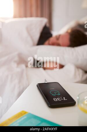 Man Asleep In Bed With Mobile Phone On Bedside Table Stock Photo