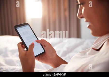 Woman Sitting Up In Bed Looking At Mobile Phone After Having Woken Up Stock Photo