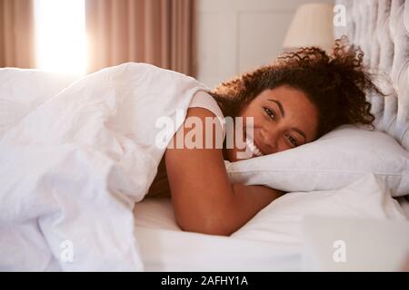 Portrait Of Woman Waking Up In Bed And Smiling At Camera Stock Photo