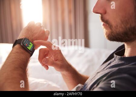 Man Sitting Up In Bed Looking At Screen Of Smart Watch Stock Photo