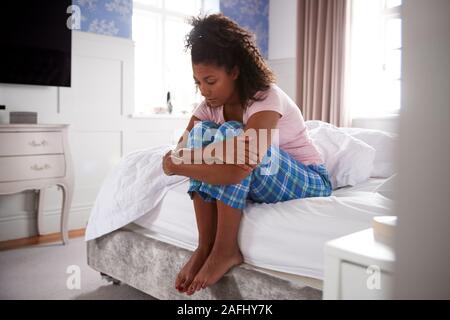 Woman Wearing Pajamas Suffering With Depression Sitting On Bed At Home