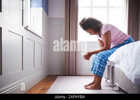 Woman Wearing Pajamas Suffering With Depression Sitting On Bed At Home Stock Photo