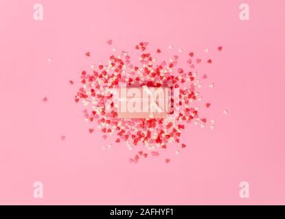 pink gift box with a bow in the center of the frame on a background of scattered little sweet candy hearts on a pink background. view from above. Stock Photo