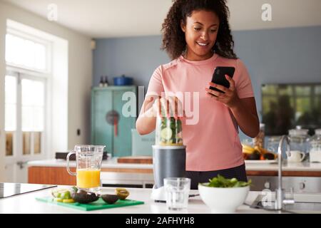 Woman Using Fitness Tracker To Count Calories For Post Workout Juice Drink He Is Making Stock Photo