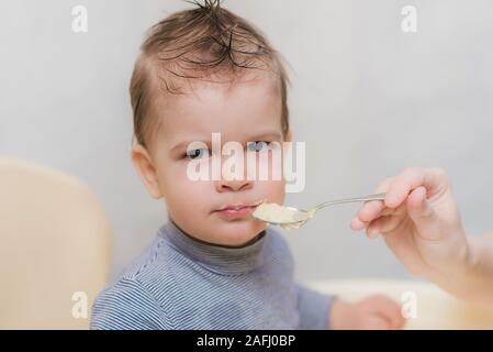 Mom feeds the child buckwheat porridge in the kitchen Stock Photo