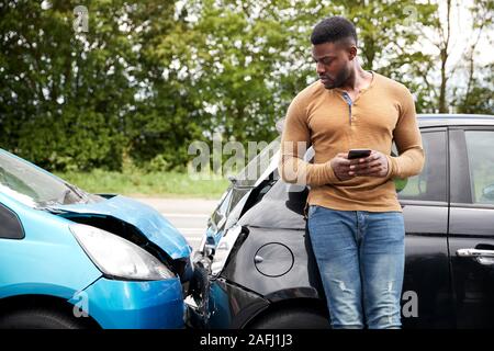Male Motorist Involved In Car Accident Calling Insurance Company Or Recovery Service Stock Photo