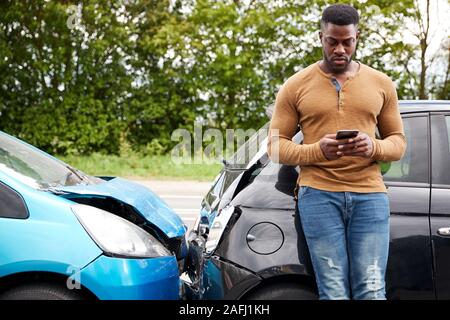 Male Motorist Involved In Car Accident Calling Insurance Company Or Recovery Service Stock Photo