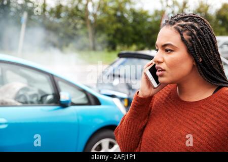 Female Motorist Involved In Car Accident Calling Insurance Company Or Recovery Service Stock Photo