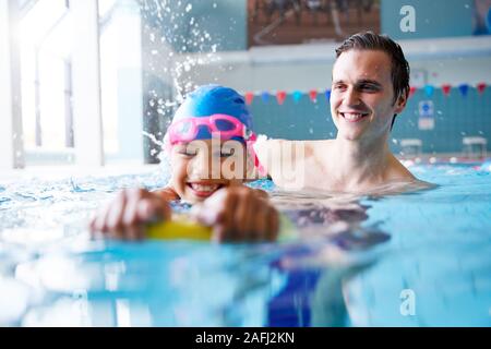 Male Swimming Coach Giving Girl Holding Float One To One Lesson In Pool