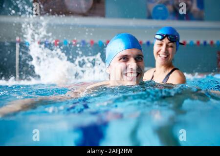 Female Swimming Teacher Giving Man One To One Lesson In Pool