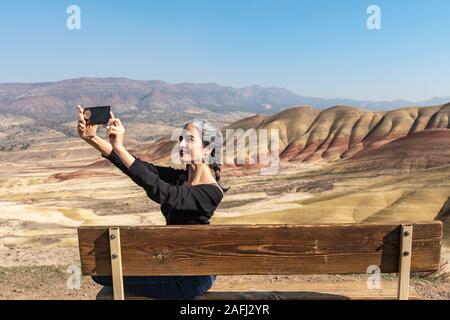 A young brunette with gray strands makes selfies sitting on a bench in Painted Hills Overlook Stock Photo