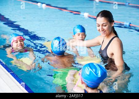 Female Coach In Water Giving Group Of Children Swimming Lesson In Indoor Pool
