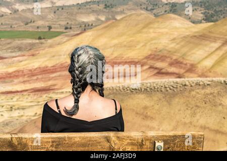 A young brunette with gray strands enjoys the view from a bench in Painted Hills Overlook Stock Photo