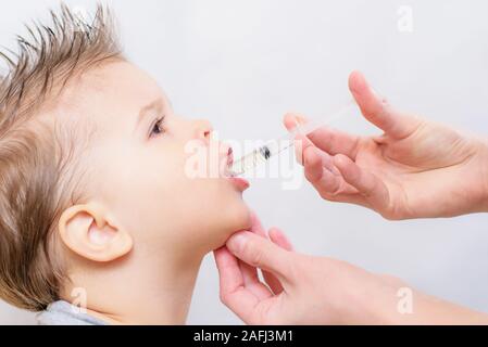 mom gives the boy fish oil through a syringe Stock Photo