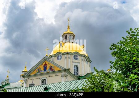 The upper part of gorgeous Baroque Orthodox Holy Dormition Cathedral in Pochayiv Lavra in Ukraine. Roof and gilded dome with a cross in the cloudy dar Stock Photo