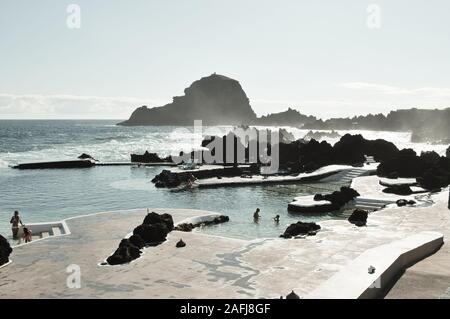Porto Moniz, Madeira, Portugal - 24 August 2019: Panoramic view of natural pools surrounded by black volcanic rock with people taking a bath in the At Stock Photo