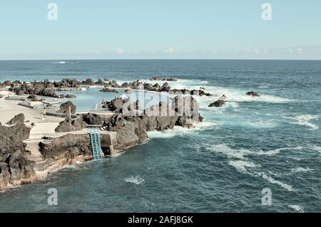 Porto Moniz, Madeira, Portugal - 24 August 2019: Panoramic view of natural pools surrounded by black volcanic rock with people taking a bath in the At Stock Photo