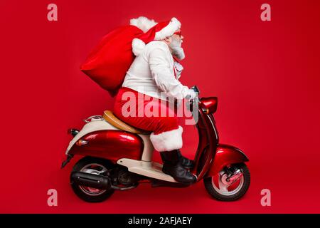 Profile side view portrait of nice bearded serious Santa Saint Nicholas father riding moped delivering big sack purchase shopping concept isolated on