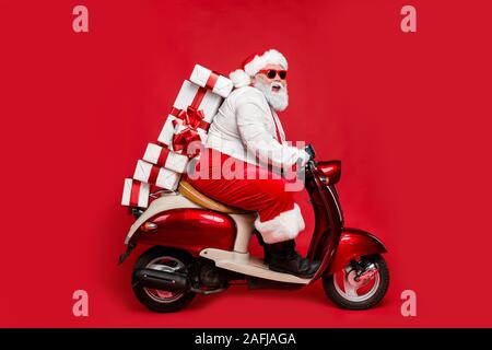 Profile side view portrait of nice bearded cheerful cheery funny funky Santa riding moped hurry up delivering pile stack winter purchases isolated on