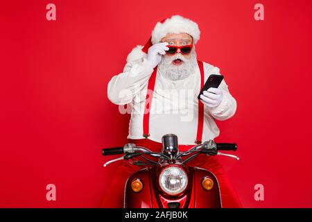 Portrait of nice attractive bearded shocked amazed funny funky Santa wearing cap hat sitting on motor bike using cell reading winter news isolated Stock Photo