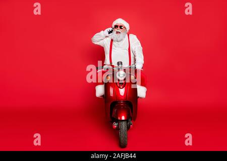 Portrait of nice attractive bearded cheerful funny Santa wearing cap hat riding motor bike talking on phone taking orders isolated over bright vivid Stock Photo