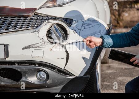 Insurance agent will examine and examine the damage to the car after an accident. Inspection of the car after an accident on the road. The front fende Stock Photo