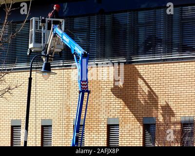 high level window cleaning. high pressure water jet. hydraulic work cage and platform on telescopic boom. brick exterior wall. worker and water hose Stock Photo