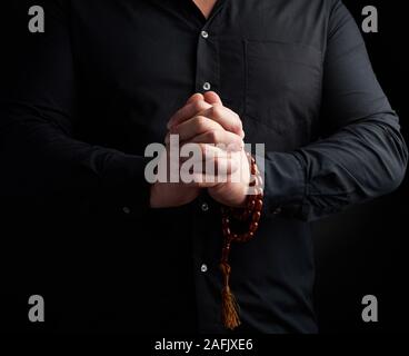 man in a black shirt joined his hands in front of his chest, prayer pose, concept of meditation and relaxation Stock Photo