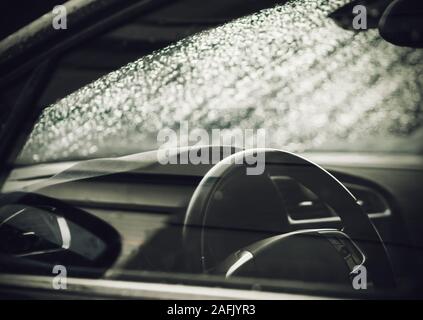 Black and white image of the car interior in rainy weather. There are a lot of water drops on the windshield. Stock Photo