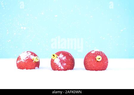 Red Christmas balls lies on the white snow with sparkles on the blue background. Christmas and New Year concept. Stock Photo
