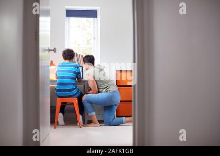 View Through Bedroom Door As Mother Helps Son Using Laptop On Desk To Do Homework Stock Photo
