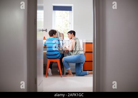 View Through Bedroom Door As Mother Helps Son Using Laptop On Desk To Do Homework Stock Photo