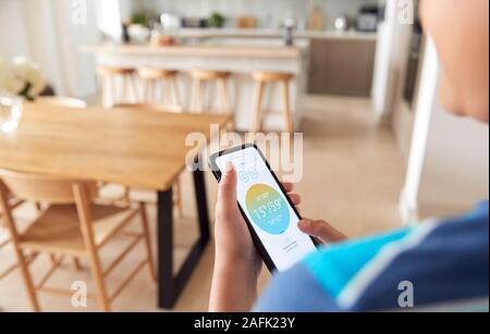 Close Up Of Boy Changing Temperature On Central Heating Thermostat Control Using Mobile Phone App Stock Photo