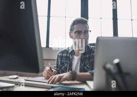 Young bearded man in eyeglasses drafting schemes Stock Photo