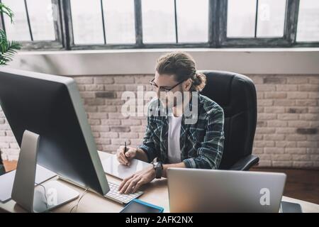 Young bearded man in eyeglasses making notes Stock Photo