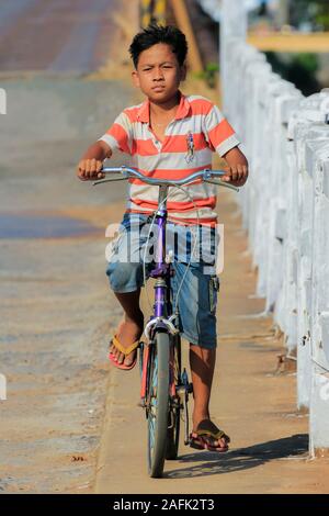 Boy riding bicycle in this old French colonial port city; Kampot, Kampot Province, Cambodia. Stock Photo