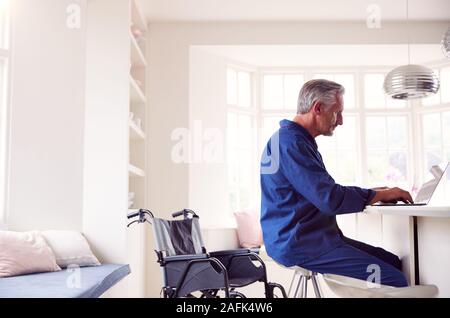 Mature Man In Wheelchair Looking Up Information About Medication Online Using Laptop Stock Photo