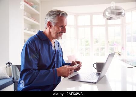 Mature Man In Wheelchair Looking Up Information About Medication Online Using Laptop Stock Photo